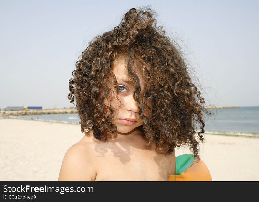 Little curly girl on the beach ready to swim in the sea.