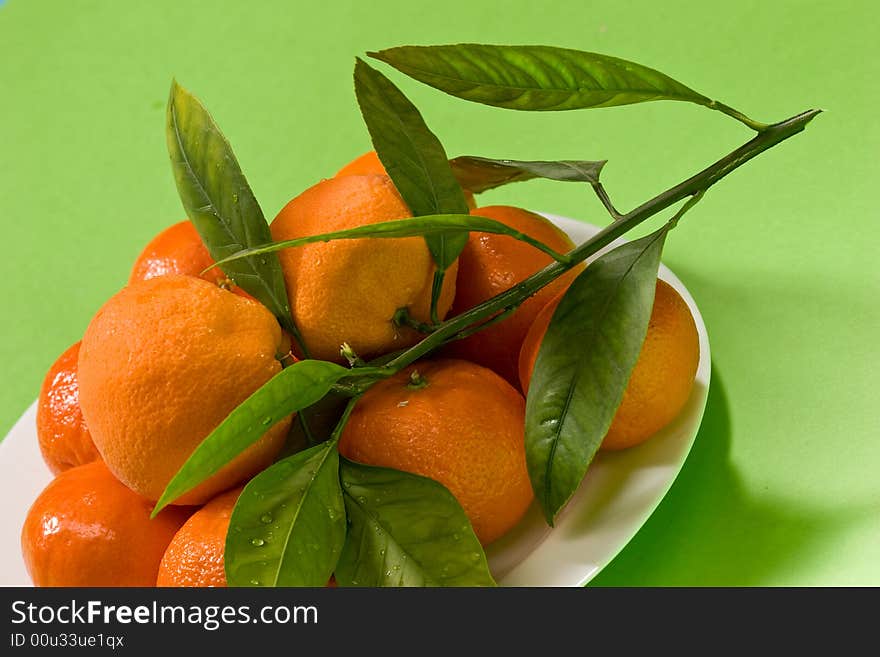 Several ripe tangerines on the plete over green background