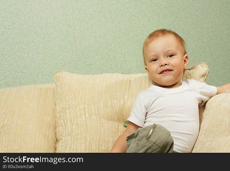 The cheerful little boy sits and on a sofa and smiles