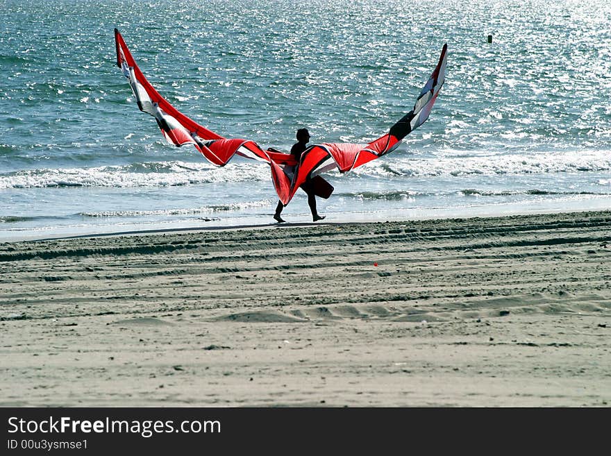 Kitesurfer walking down a beach after exhausting workout. Kitesurfer walking down a beach after exhausting workout.