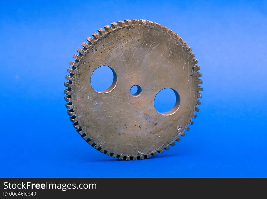 Old perforated and scratched cogwheel against the blue background.