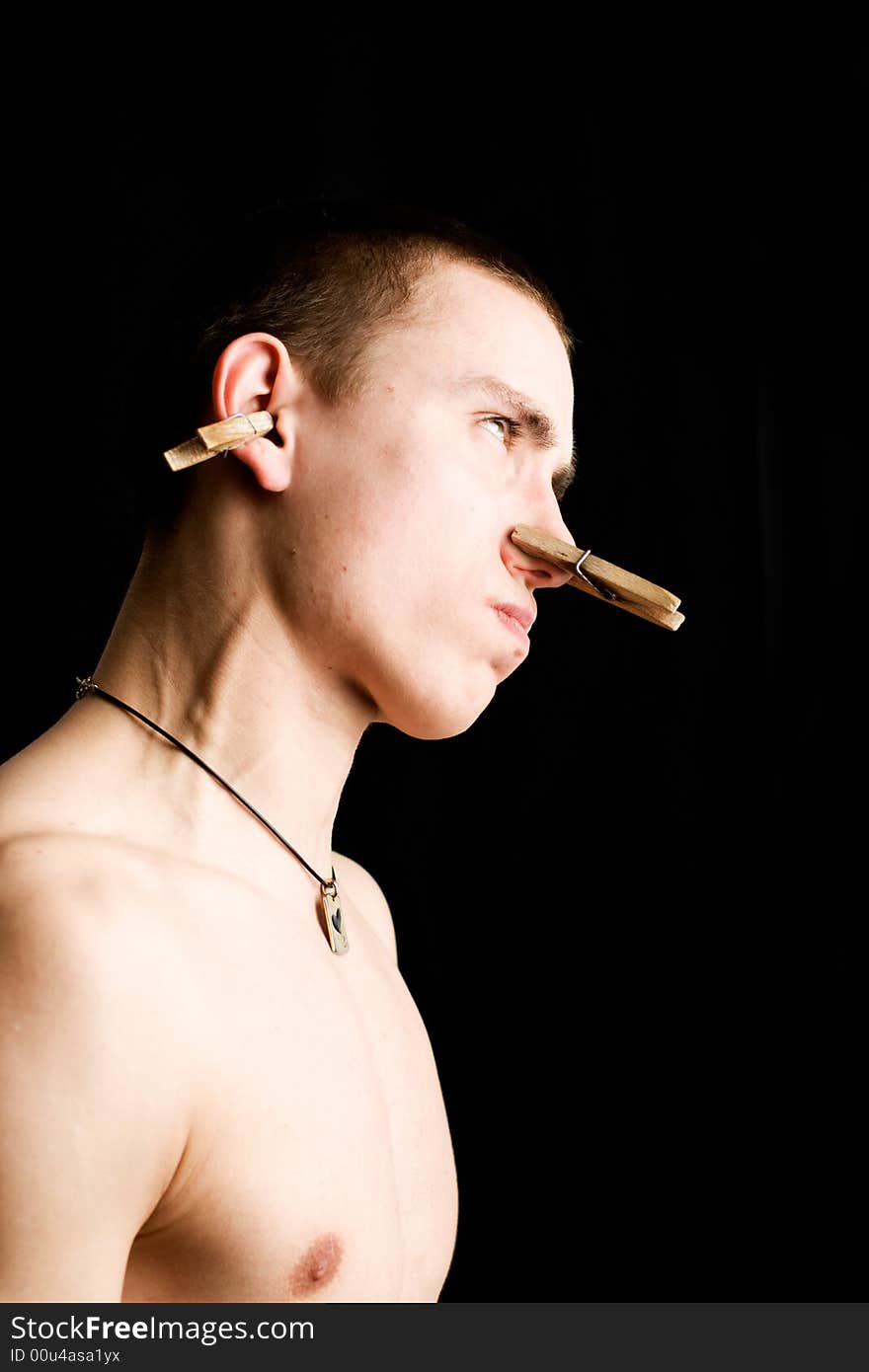 Furious man with clothes-peg on his nose and ear. Isolated on black.