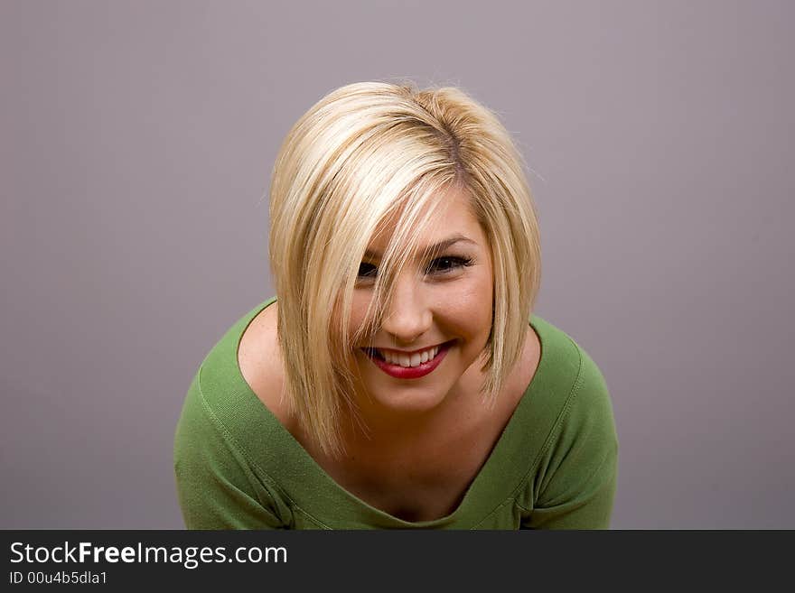 A blonde in a green blouse leaning forward and smiling at the camera. A blonde in a green blouse leaning forward and smiling at the camera