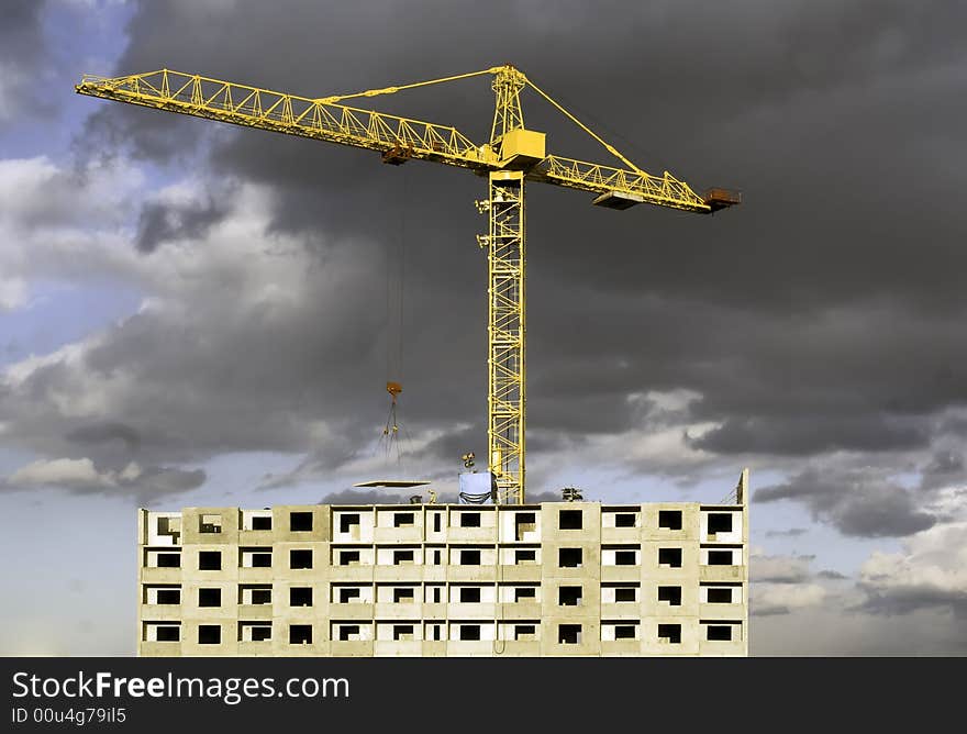 Hoisting crane lifting a concrete slab on a house being built, on the background of gloomy thunder clouds. Hoisting crane lifting a concrete slab on a house being built, on the background of gloomy thunder clouds