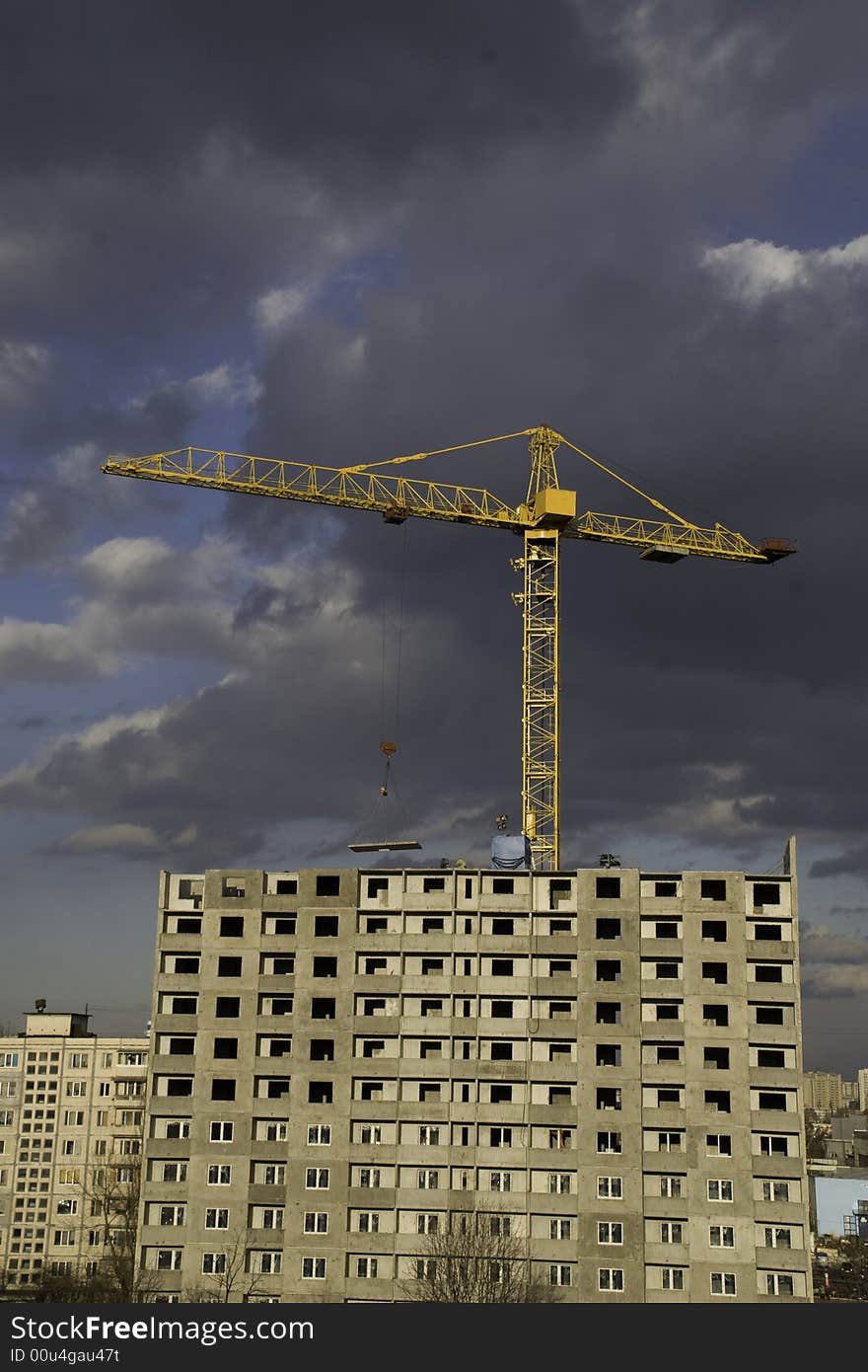 Hoisting crane lifting a concrete slab on a house being built, on the background of gloomy thunder clouds. Hoisting crane lifting a concrete slab on a house being built, on the background of gloomy thunder clouds