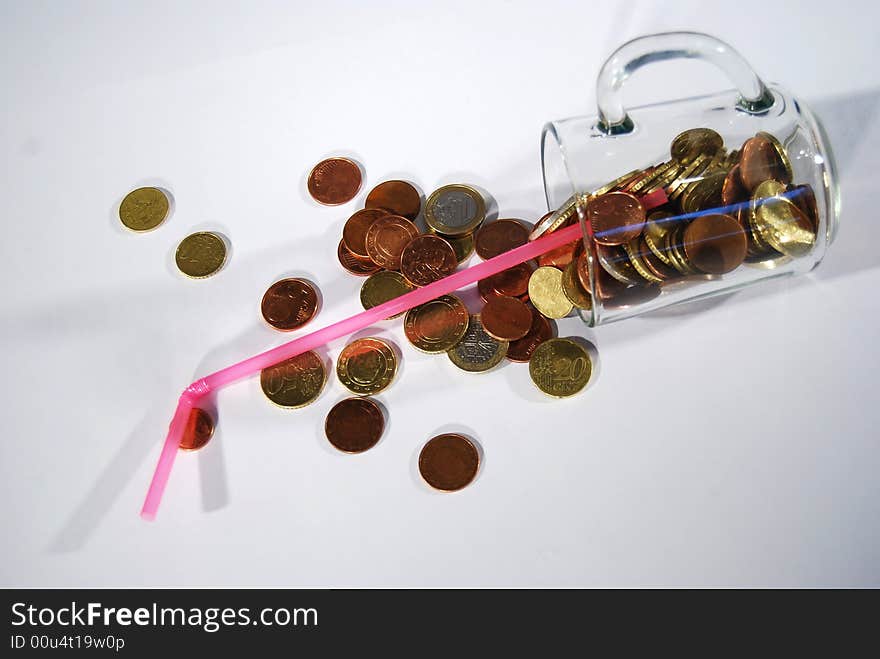 A glass filled with change and a straw falls down and spills the money. A glass filled with change and a straw falls down and spills the money