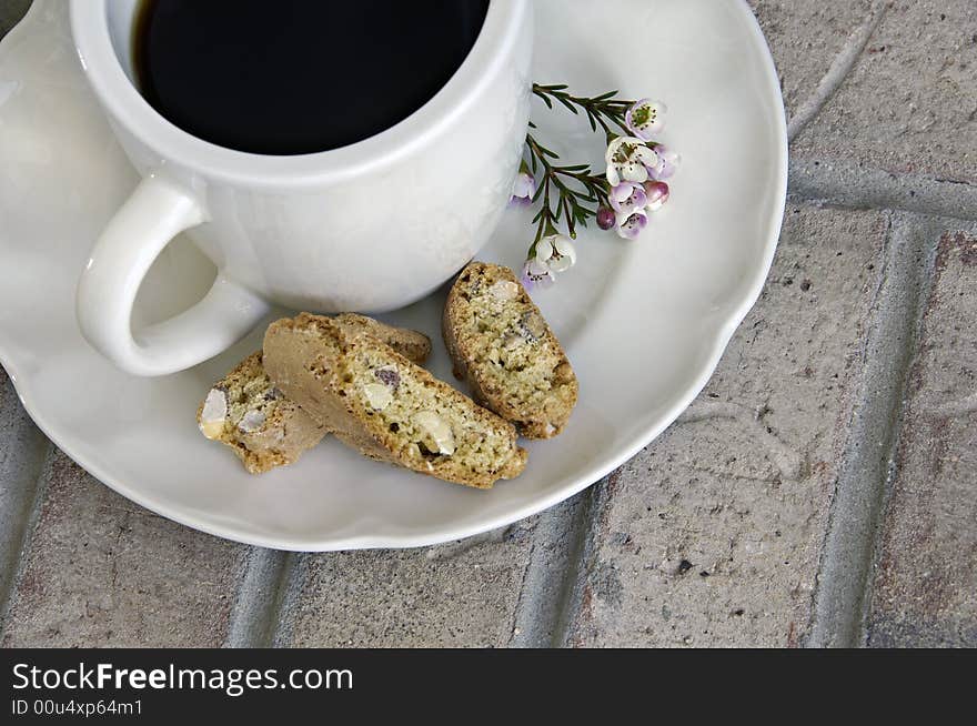 Cup of coffee with biscotti and small flowers on a brick background. Cup of coffee with biscotti and small flowers on a brick background.