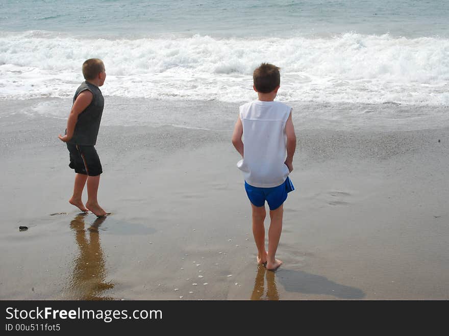 Two barefooted boys face the ocean, waiting to race the cold waves ashore. One boy is on his toes in expectation. Two barefooted boys face the ocean, waiting to race the cold waves ashore. One boy is on his toes in expectation.