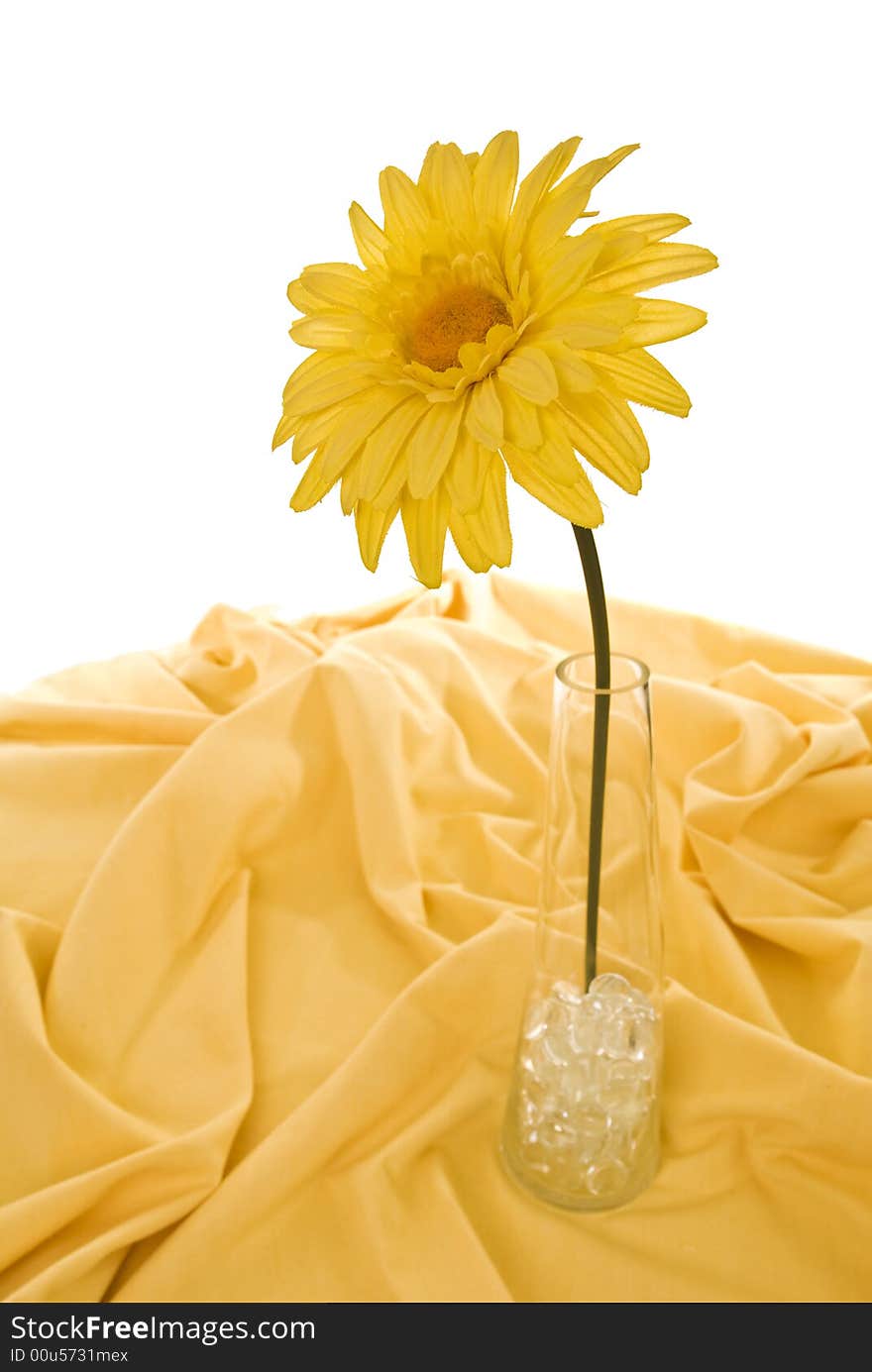 Cloth sunflower in glass vase with glass pebbles on yellow tablecloth, isolated on white.