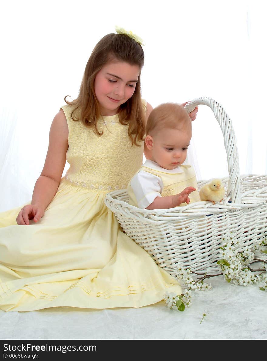 Smiling school aged girl and baby brother sitting in basket, looking at yellow chick. Smiling school aged girl and baby brother sitting in basket, looking at yellow chick