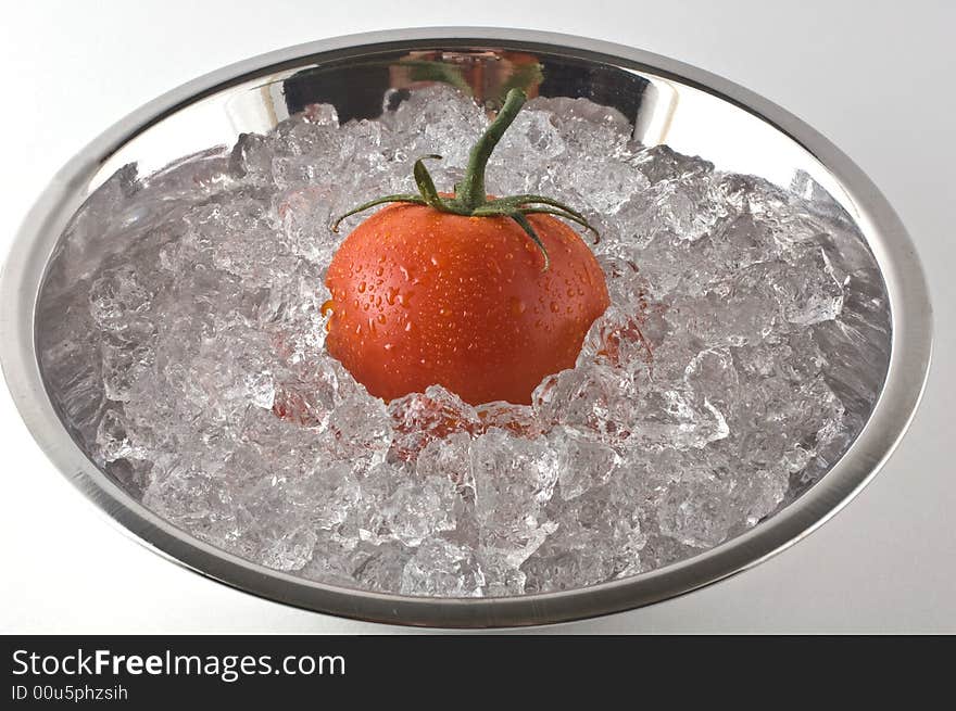 Bright red tomato resting in metal bowl of ice isolated on white. Bright red tomato resting in metal bowl of ice isolated on white