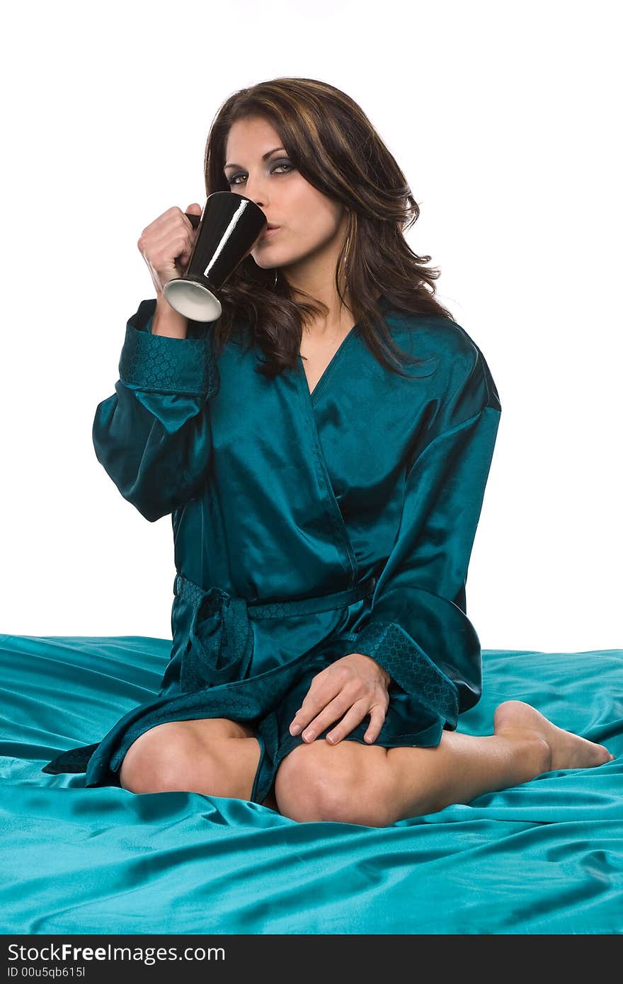 Pretty brunette sitting on green satin sheets in green satin robe relaxing and drinking coffee from cup. Pretty brunette sitting on green satin sheets in green satin robe relaxing and drinking coffee from cup