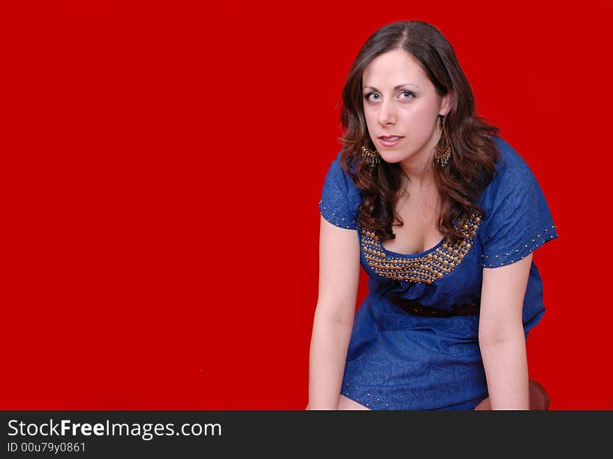 Portrait of attractive young lady kneeling in blue dress on red background. Portrait of attractive young lady kneeling in blue dress on red background