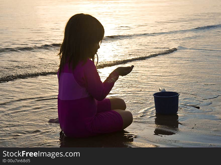 Girl playing with the sand on the beach at sunset. Girl playing with the sand on the beach at sunset