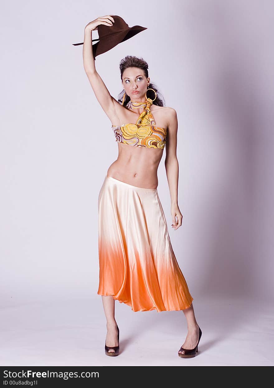 Young woman wearing a colorful top and flowing skirt holding an old hat over her head. Young woman wearing a colorful top and flowing skirt holding an old hat over her head