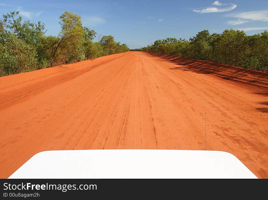 Red Australian rural road with blue sky. Perspective from the car hood. Copy space. Red Australian rural road with blue sky. Perspective from the car hood. Copy space.