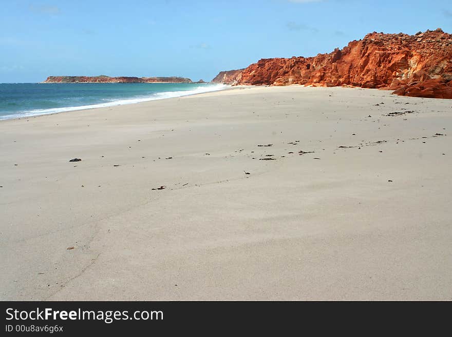 Blue clear sky over the red rocks on a long sandy beach. Australian. Blue clear sky over the red rocks on a long sandy beach. Australian