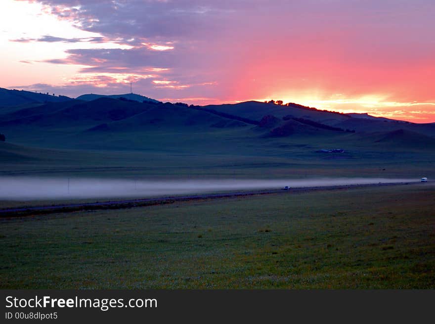 Bloody sky at sunrise with mountain line.Fog on road. Bloody sky at sunrise with mountain line.Fog on road.