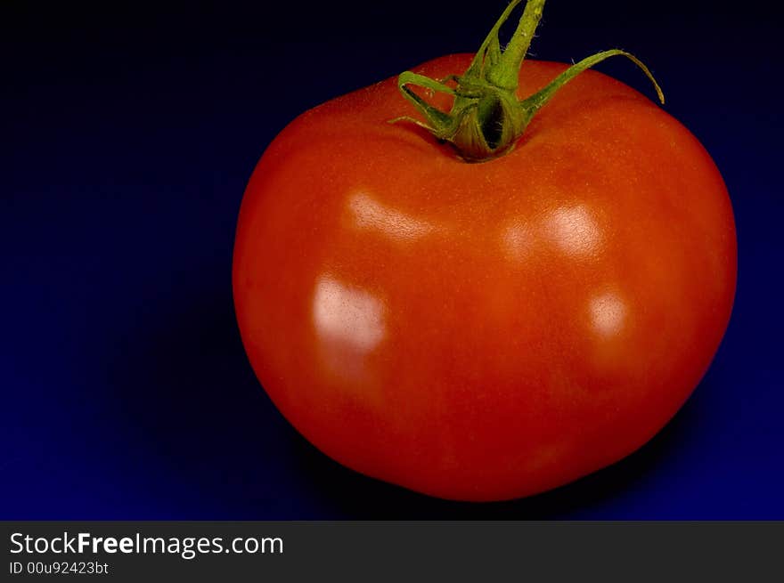 Big red tomato on blue with dark background