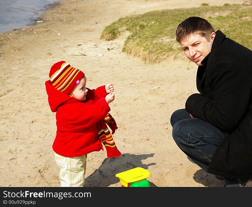 Daddy with a daughter play with sand on coast of lake