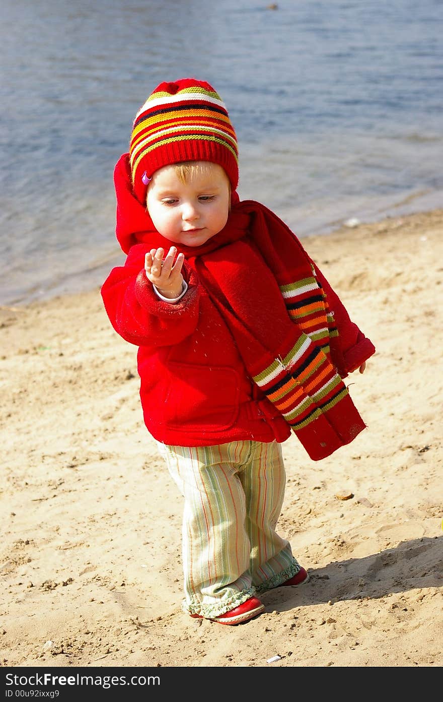 Little girl plays with sand on coast of lake