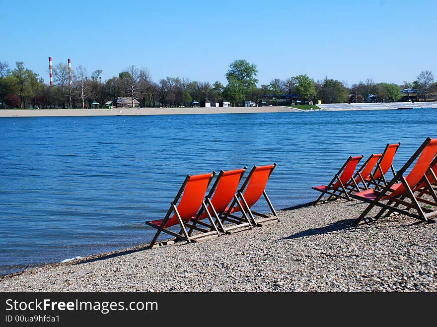 Empty orange folding chairs by blue lake. Empty orange folding chairs by blue lake