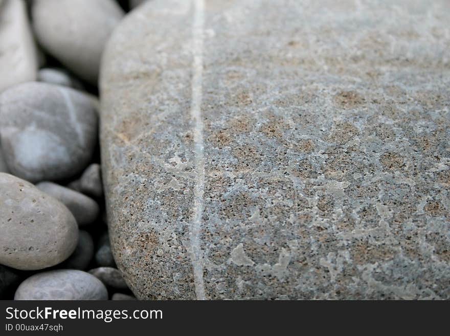 Grey pebbles background, a big one with a white stripe and several small ones