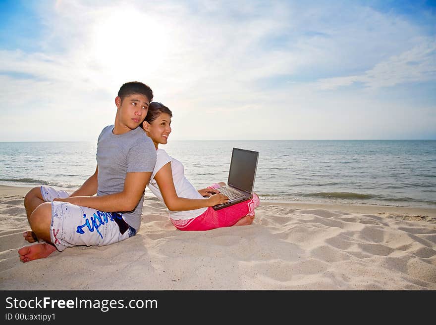 Couple relaxing on the beach while one of them haapily working on laptop. Couple relaxing on the beach while one of them haapily working on laptop