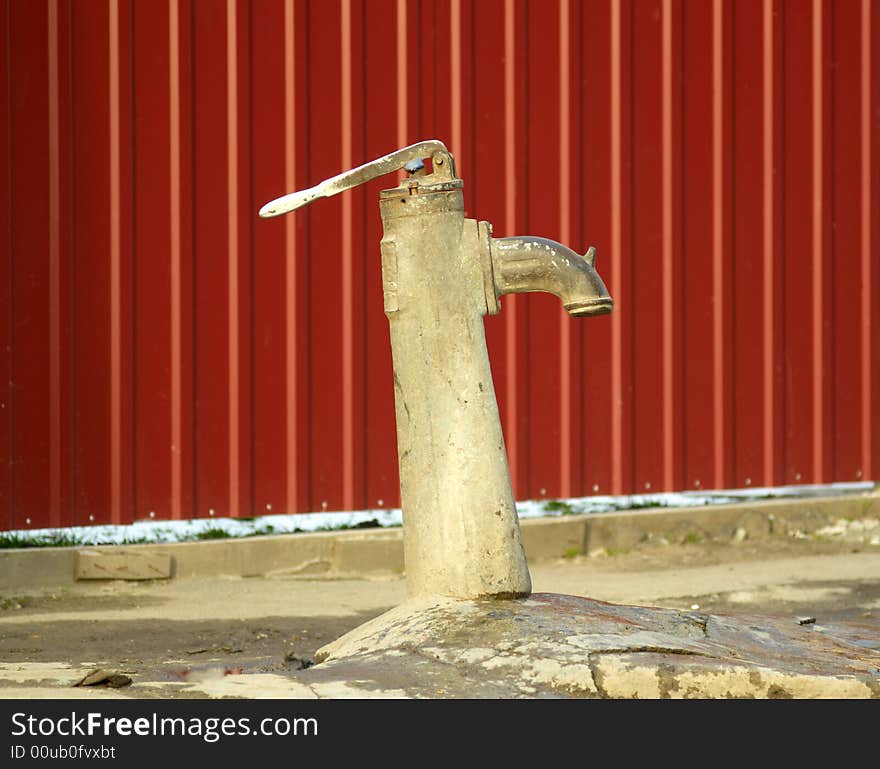 The old water pump on a background of a red wall