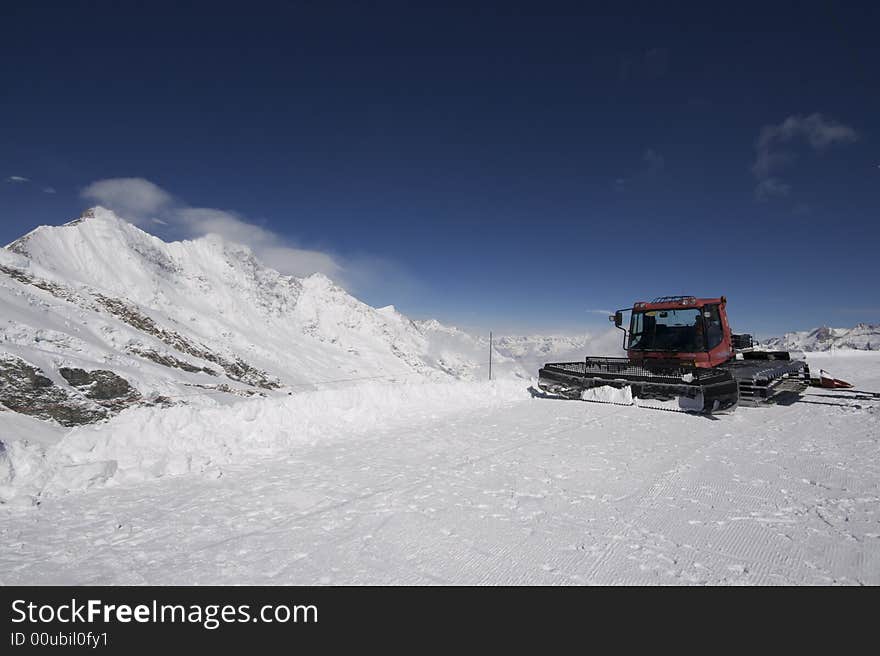 This photograph shows the top of a mountain in the resort of Saas-Fee in Switzerland. There are ski marks in the snow, and there is a piste basher in the frame showing the ski slope area. This photograph shows the top of a mountain in the resort of Saas-Fee in Switzerland. There are ski marks in the snow, and there is a piste basher in the frame showing the ski slope area.