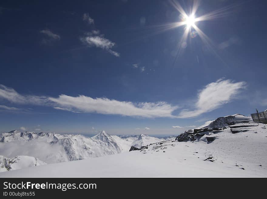 This photograph shows the top of a mountain in the resort of Saas-Fee in Switzerland. There are ski marks in the snow, and you can see down the valley over Saas-Fee and other mountain villages. This photograph shows the top of a mountain in the resort of Saas-Fee in Switzerland. There are ski marks in the snow, and you can see down the valley over Saas-Fee and other mountain villages.