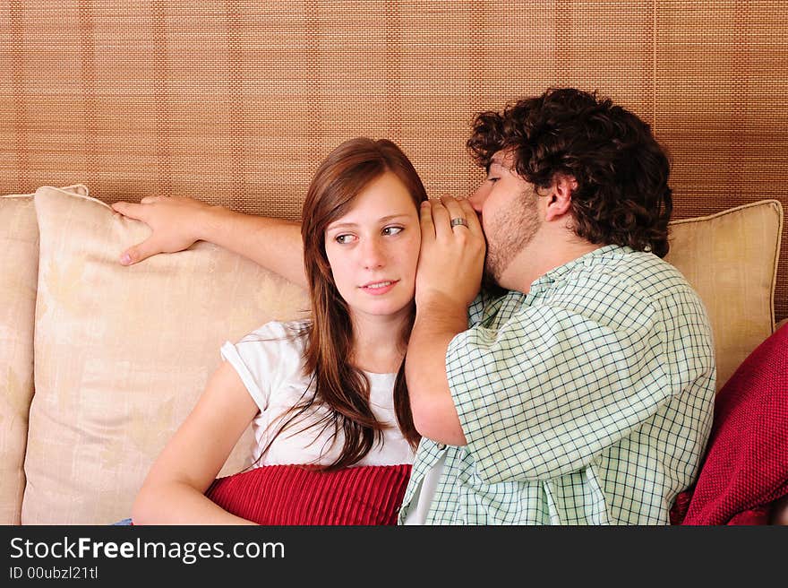 Young couple relaxing on a couch. Boy whispering into the girls' ear. Young couple relaxing on a couch. Boy whispering into the girls' ear.