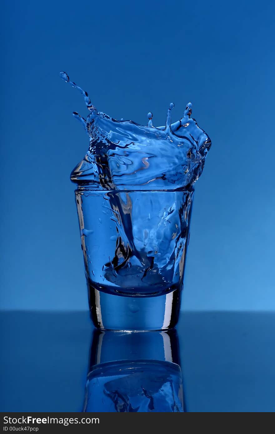 Glass with splashing water over  blue