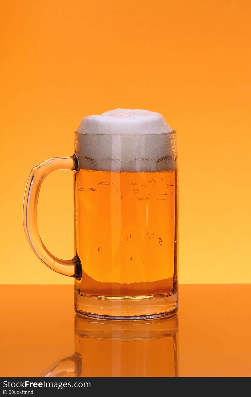 Mug of beer with froth over orange background