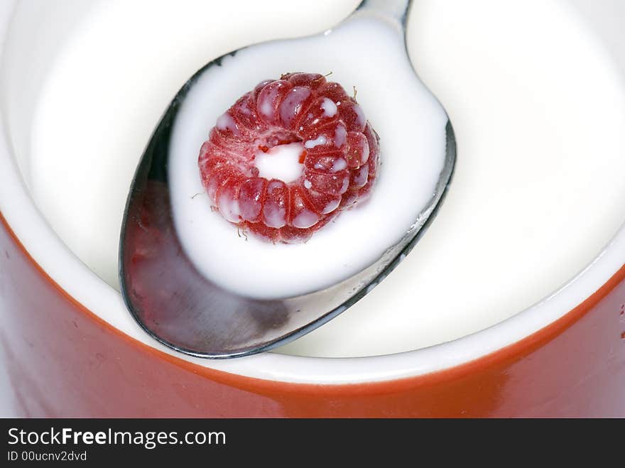 Raspberry on a spoon with a cup full of milk