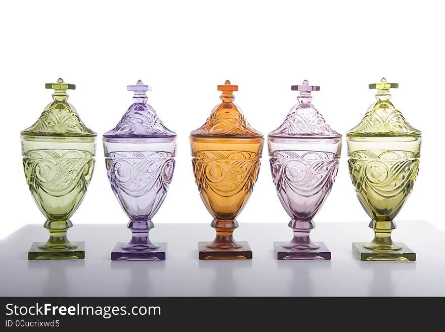 Five crystal candy jars in different colors on grey table against white background. Five crystal candy jars in different colors on grey table against white background