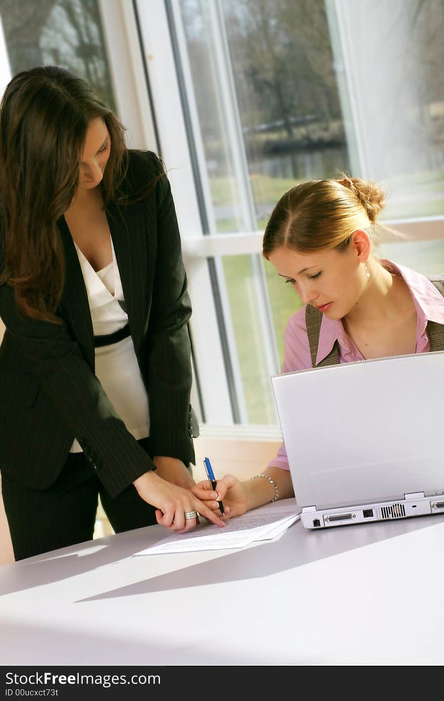 A successful business woman and her secretary with a document on a table with a laptop