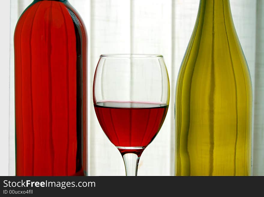 Bottles of red and white wine with a wine glass in between. Bottles of red and white wine with a wine glass in between
