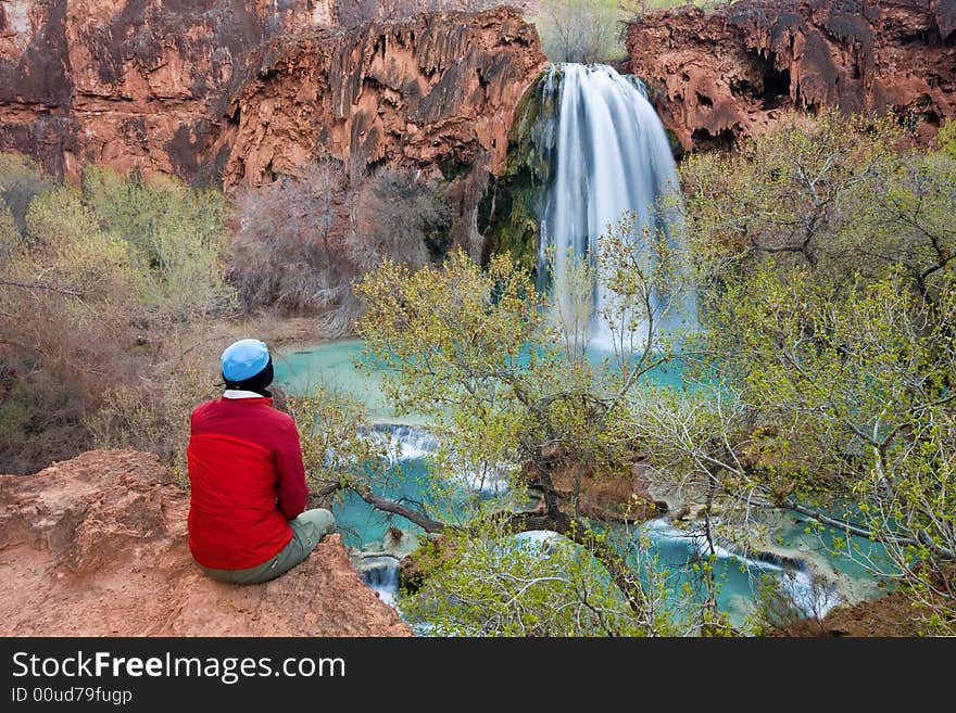 Woman sitting at the edge of a cliff watching Havasu Falls drop into it's turquoise pool. Havasu Canyon, Arizona. Havsupai Reservation. Woman sitting at the edge of a cliff watching Havasu Falls drop into it's turquoise pool. Havasu Canyon, Arizona. Havsupai Reservation.