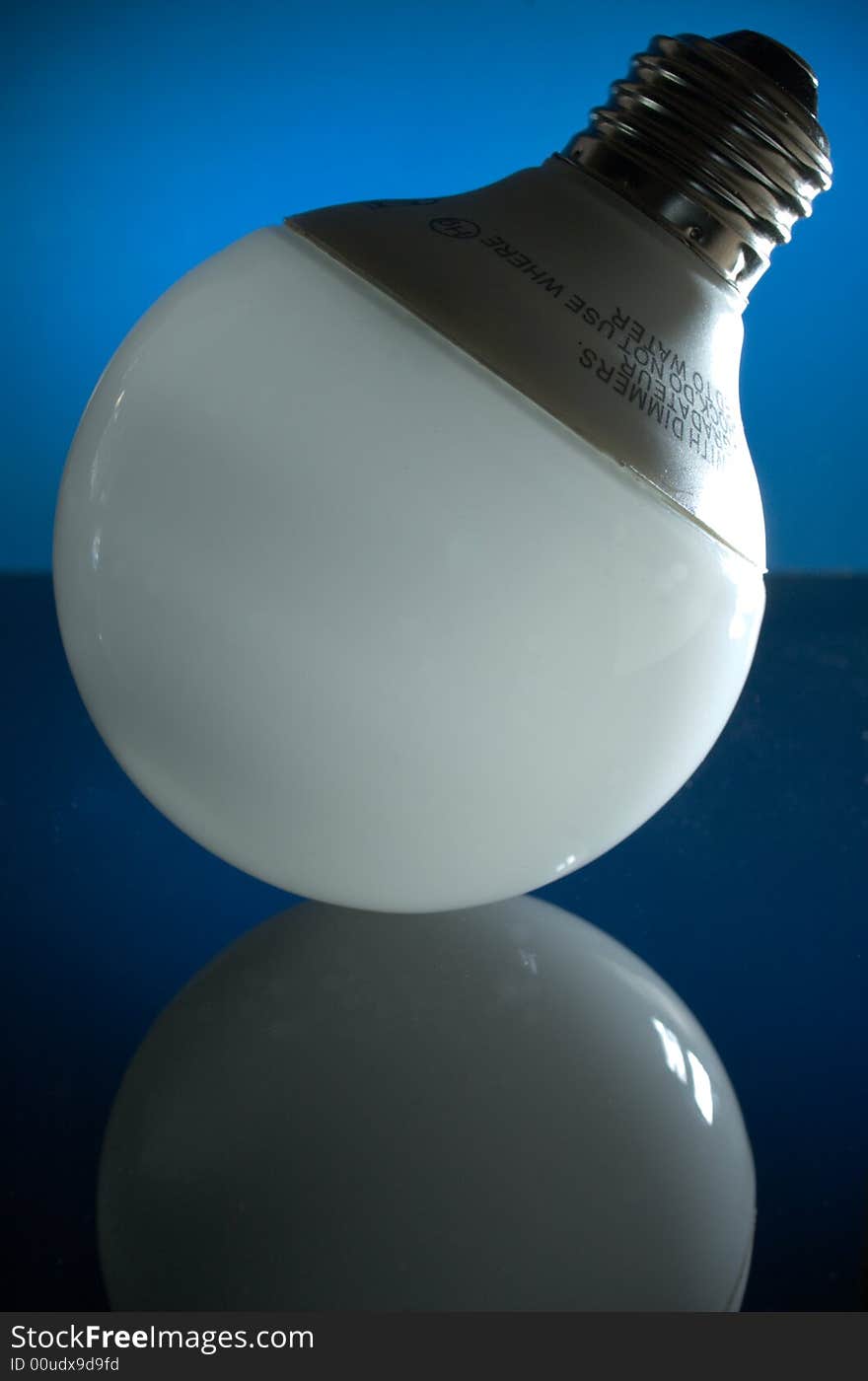 A CFL globe lamp, standing with its base pointing upward, on a dark reflective surface with a blue illuminated background.