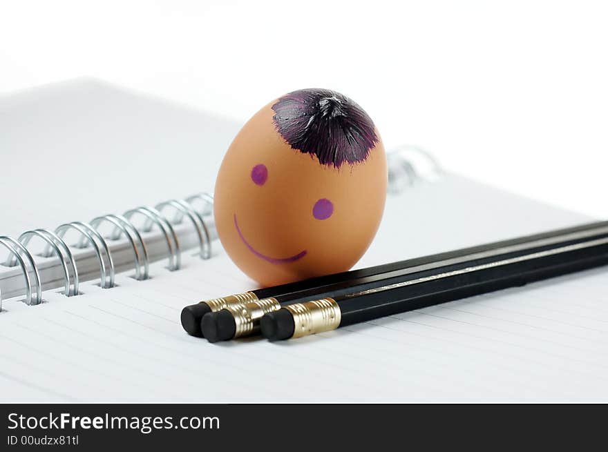 Smiley egg with black pencils on note book. Smiley egg with black pencils on note book