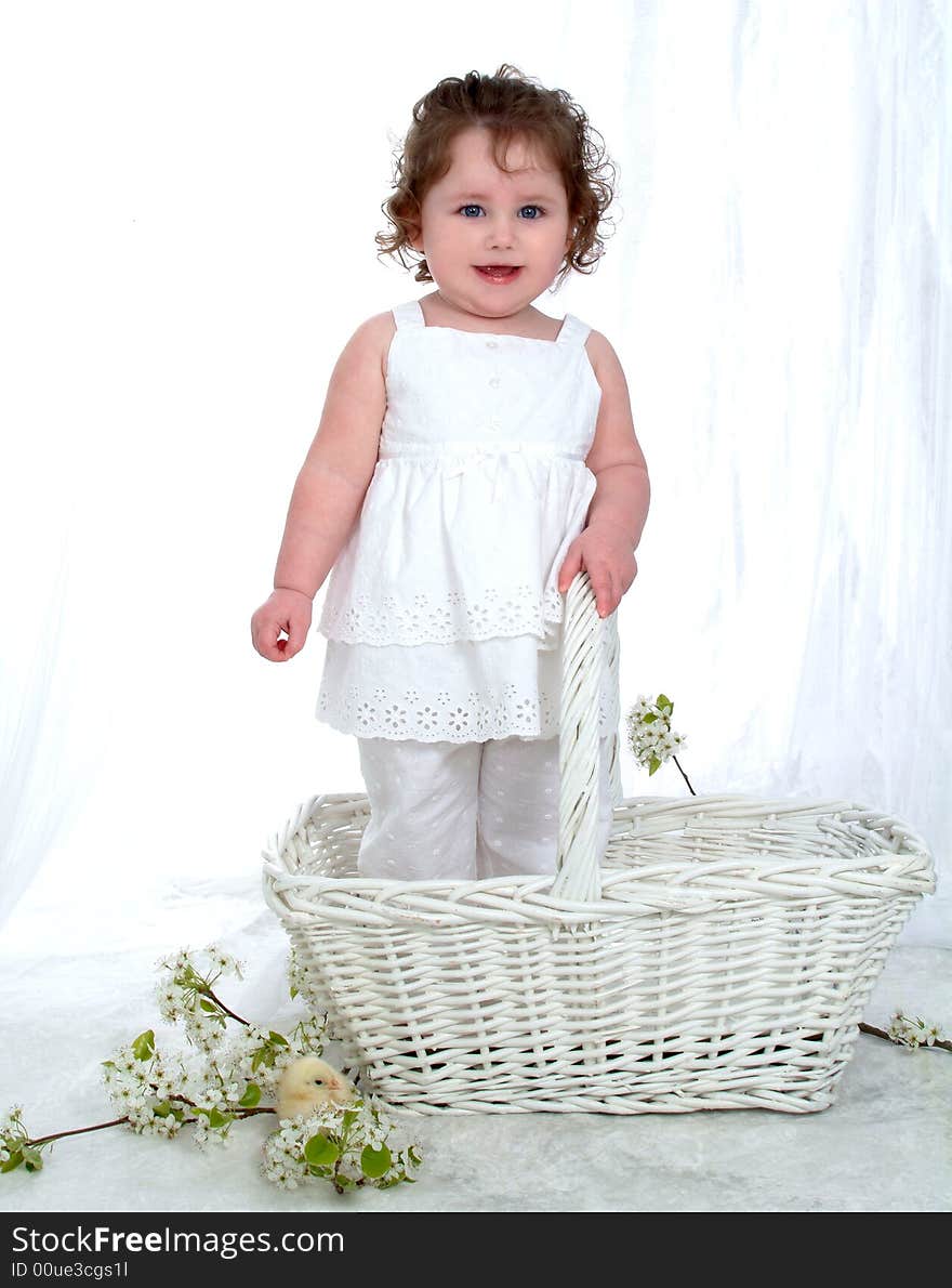 Baby girl in wicker basket in front of white background with flowers on floor and chick perched on flowers. Baby girl in wicker basket in front of white background with flowers on floor and chick perched on flowers