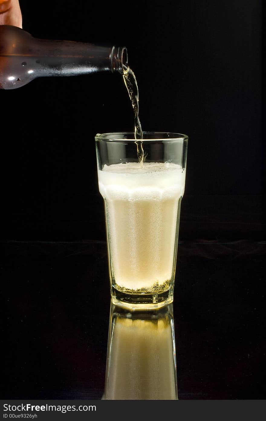 Pouring an ice-cold beer into a glass, isolated against black with reflection. Pouring an ice-cold beer into a glass, isolated against black with reflection