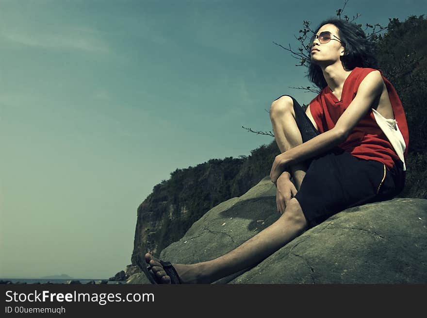 Young man sitting on rock by the beach. Young man sitting on rock by the beach