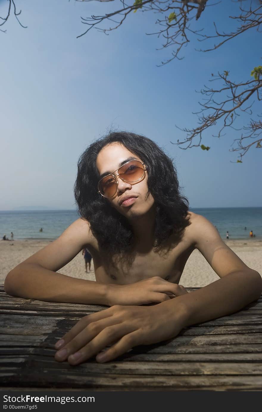 Young man sitting on bamboo bench at beach. Young man sitting on bamboo bench at beach