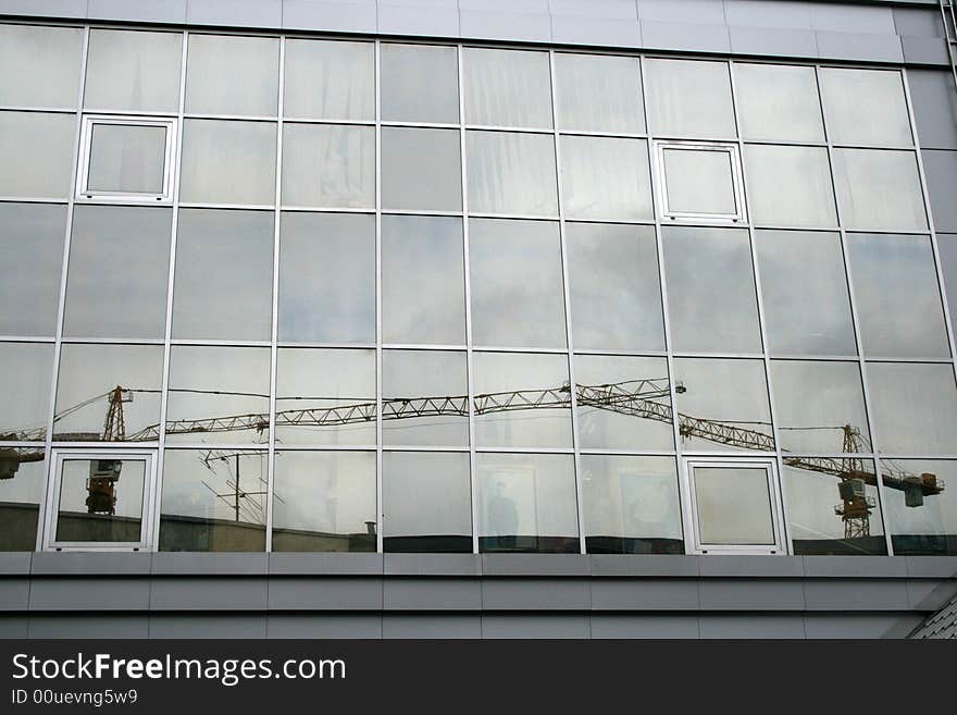 Reflection of the lifting cranes in the window of the business center