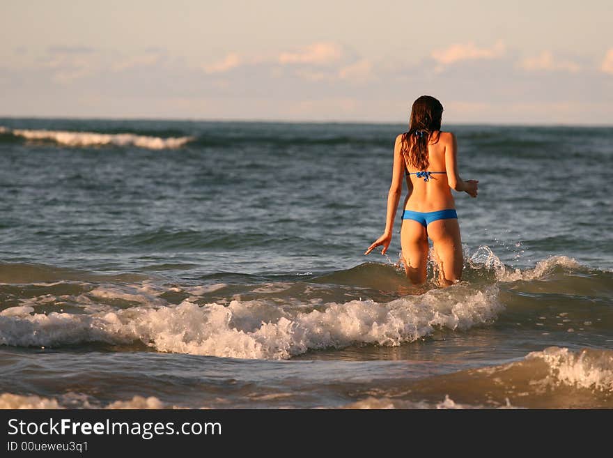 Young woman goes in ocean to swim by sunset. Young woman goes in ocean to swim by sunset