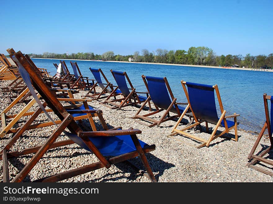 Blue folder chairs row on stone beach by lake. Blue folder chairs row on stone beach by lake