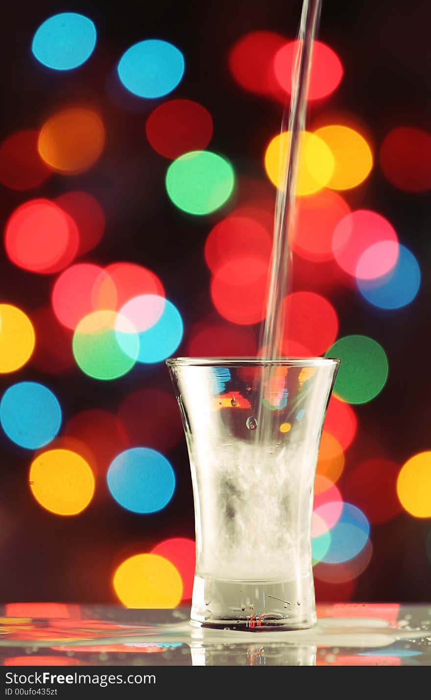 Pouring a seethrough liquid in to a shot glass, fairy light background, please check for more. Pouring a seethrough liquid in to a shot glass, fairy light background, please check for more