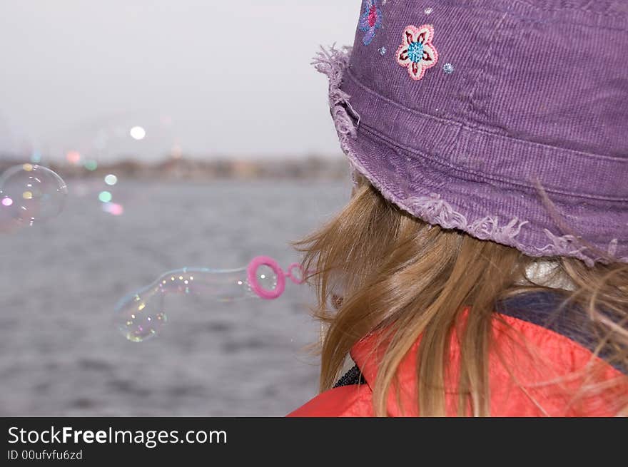 Child blowing soap bubbles out on the river bank